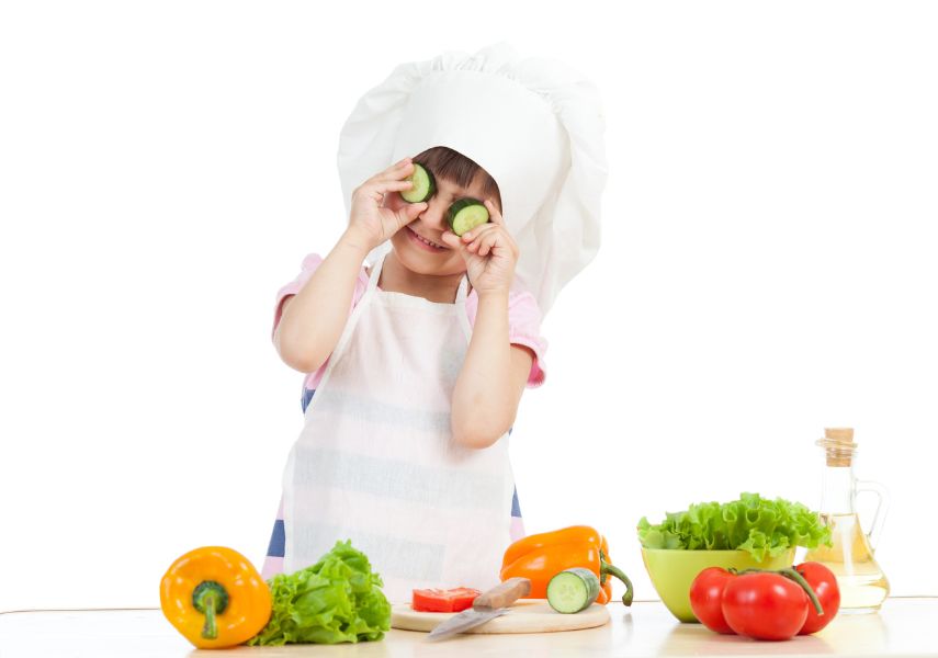 Barn med kockkniv, skär grönsaker, håller två gurkskivor över ögonen