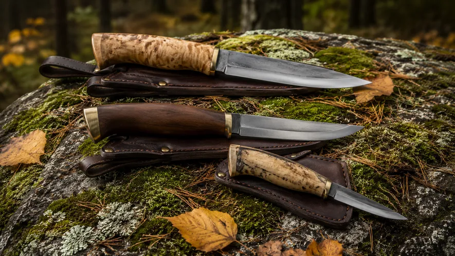 Svenska friluftsknivar med trähandtag upplagda på mossig sten i skogen